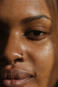 A detailed close-up of a woman's face highlighting her skin texture and nose ring.